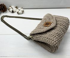 a crocheted purse sitting on top of a white table next to a pine cone