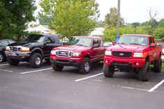 three pickup trucks parked in a parking lot next to each other with trees and grass behind them