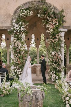 a bride and groom standing in front of an arch with flowers on it at their wedding ceremony