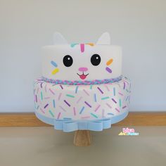 a white cake with sprinkles and a cat on top