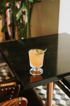 a drink sitting on top of a black table next to a brown chair and potted plant