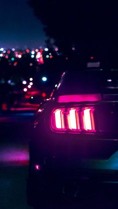 the back end of a car at night with its lights on and city lights in the background