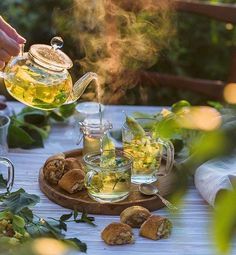 a person pouring tea into a glass pitcher on top of a wooden table surrounded by greenery