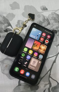 an iphone with a keychain attached to it sitting on a floral print sheet