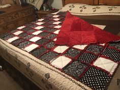 a bed with a red and black quilt on it's cover, sitting next to a dresser