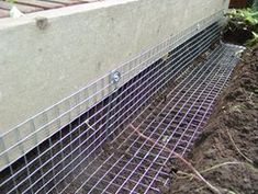 a close up of a wire mesh fence on the side of a building with dirt in front of it