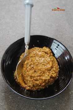 a black bowl filled with food sitting on top of a gray counter next to a spoon