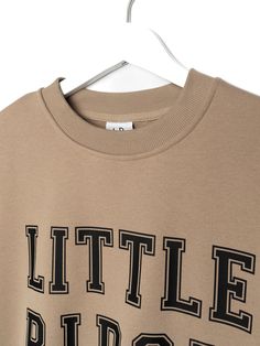 Calling all LB superfans! The most stylish way to show your LB pride is our Collegiate Crewneck, featuring classic 'Little Bipsy' text + the familiar, cozy feel of your favorite college sweatshirt. Pair it with our Athletic Ribbed Biker Short or Legging to rep LB from head to toe! Color: Tan 'LITTLE BIPSY' printed on the front Ribbed neckline, cuffs, and bottom hem Rollable + cinched wrist cuffs Material + Wash: 86.7% cotton | 13.3% polyester Do not bleach Machine wash cold with like colors Dry Fall Varsity T-shirt With Logo Print, Collegiate Logo Print Sweatshirt For Fall, Urban Slogan Tops For Fall, Fall Loungewear Sweatshirt With Logo Print, Fall College Sweatshirt With Logo Print, College Logo Print Sweatshirt For Fall, College Style Sweatshirt With Logo Print And Crew Neck, Fall College Logo Print Sweatshirt, Winter Slogan Tops For College