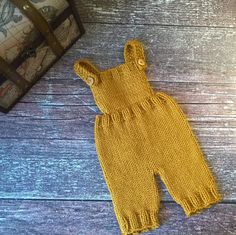 a yellow knitted baby's outfit next to a suitcase on a wooden floor