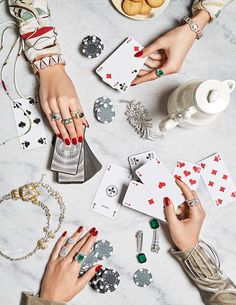 two hands holding playing cards on top of a table with bracelets and other accessories