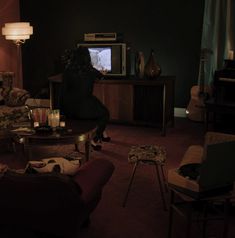 a person sitting on a couch watching tv in a dark room with two chairs and a coffee table