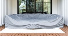 a couch covered in a gray cover sitting on top of a wooden floor next to a window