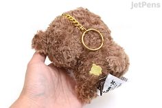 a hand holding a brown teddy bear with a gold keychain on it's back