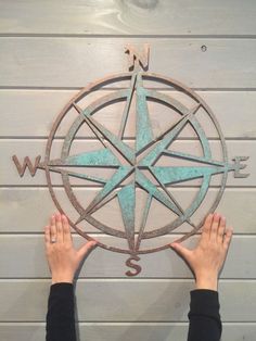 two hands are reaching up towards a metal compass on a white wooden wall with planks