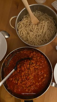 two pans filled with pasta and sauce on top of a wooden table next to plates