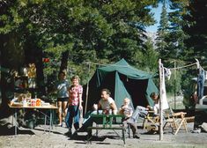 a group of people standing around a green table in the grass with tents behind them