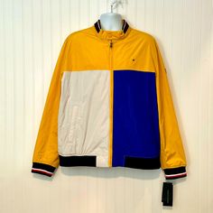 Classic Yellow & Blue Colorblock Lightweight Varsity Bomber Jacket From Tommy Hilfiger In Men's Size Xxl (2xl). Measurements: 56" Chest | 54" Waist | 48-56" (Stretchy) Hem/Hips | 29" Length | 28" Sleeves. Men's Jacket Is Colorblocked With Yellow, White And Blue Colors. Full Zip Front. Classic Bomber Jacket Style With Stretchy Banded Hem And Sleeve Cuffs. Hem Is Navy Rib Knit. Sleeves Are Striped Rib Knit. Long Sleeve Length. Logo On The Chest And On The Left Sleeve. Stand Collar -- Rib Knit On T Winter Yellow Color Block Outerwear, Long Sleeve Yellow Color Block Outerwear, Yellow Color Block Outerwear For Spring, Spring Yellow Color Block Outerwear, Vintage Tommy Hilfiger Jackets, Military Style Jackets, Tommy Hilfiger Jackets, Blue Jean Jacket, Tommy Hilfiger Sweater