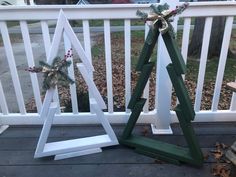 two wooden christmas trees sitting on top of a porch next to a white picket fence