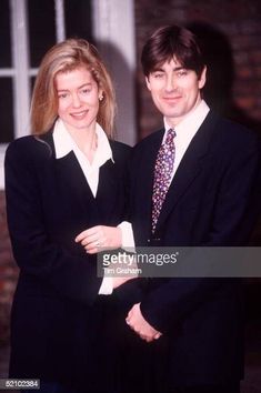 a man and woman standing next to each other in front of a brick wall with windows