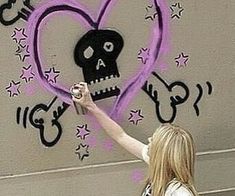 a woman is painting a wall with purple spray paint and a skull in the shape of a heart