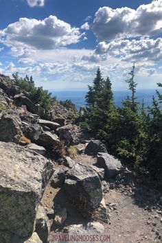 a rocky trail with trees on the side and clouds in the sky above it that is covered by rocks