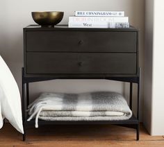 a nightstand with two books on it next to a white bed and a black night stand