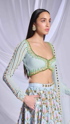 Like a breath of fresh air, our ice blue sequin-printed lehenga comes with pockets! Adorned with opulent gold embellishments, pearls, crystals and 3d flowers. Paired with a full-sleeve embroidered blouse with pearls, crystals, pink enamelled drops and glass stones along with a matching tulle dupatta filled with acrylics, crystals and a pearl border. Light Blue Sets With Sheer Dupatta For Diwali, Festive Light Blue Set With Sheer Dupatta, Blue Hand Embellished Choli For Reception, Festive Light Blue Sharara For Reception, Blue Hand Embellished Choli With Traditional Drape, Hand Embellished Blue Choli With Traditional Drape, Bollywood Style Hand Embellished Blue Sets, Traditional Blue Hand Embellished Choli, Festive Blue Hand Embellished Choli