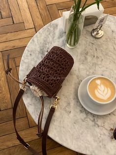 a cup of coffee on a marble table with a crocheted purse and sunglasses