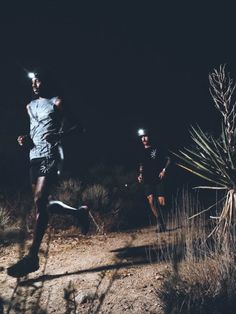 two men running in the dark with their headlamps on and one man is wearing a hat