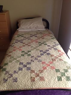 a bed with a quilt on top of it next to a night stand and dresser