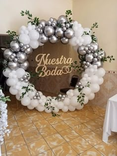 a balloon arch with silver and white balloons in the shape of a wreath that reads, meestra bada