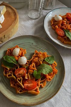 two plates of pasta with tomatoes, basil and cheese on them sitting on a table