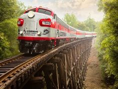 a red and white train traveling over a wooden bridge in the middle of some trees