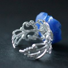 "A handmade cobalt blue resin rose has then been set upon an silver plated filigree adjustable ring base in your choice of finish in this romantic flower ring that is made to be adjustable from size 6 and up. Flower Size: 19mm To see this ring in all available colors, check here: http://etsy.me/1gr9dLc The base for this handmade ring is adjustable, which makes this delicate rose ring comfortable no matter the size of the wearer's fingers (size 6 and up) as well as ideal for switching from finger Adjustable Blue Flower Ring For Gifting, Blue Flower Ring For Gift, Adjustable Blue Flower Ring Gift, Unique Blue Flower Ring For Gift, Elegant Adjustable Blue Flower Ring, Elegant Blue Adjustable Flower Ring, Handmade Blue Flower Ring, Adjustable Blue Flower Ring, Blue Flower-shaped Jewelry For Her