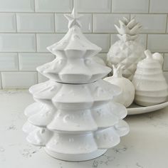 three white ceramic christmas trees sitting on top of a counter next to a plate and bowl