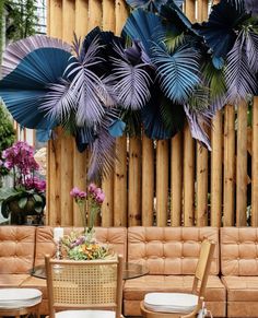 a living room filled with lots of furniture next to a wooden wall covered in purple and green leaves