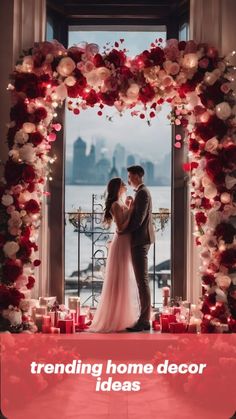 a man and woman standing in front of a window surrounded by red flowers with candles