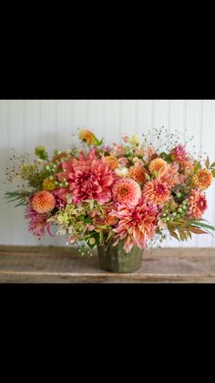 a vase filled with lots of colorful flowers on top of a wooden table next to a white wall