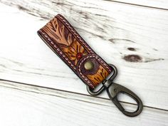 a leather keychain with a metal clip on it's side and an orange flower in the center