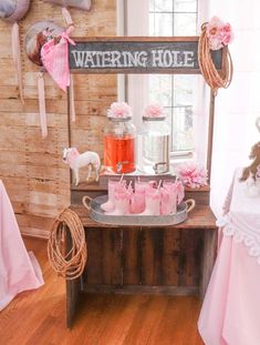 a table topped with pink cups filled with water and other items next to a window