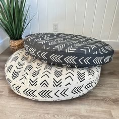 two black and white pillows sitting on top of each other next to a potted plant