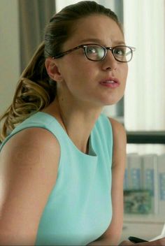 a woman wearing glasses sitting at a desk in front of a laptop computer and looking off to the side