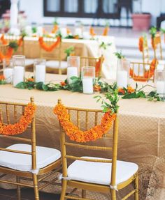 the chairs are decorated with orange flowers and greenery, along with candles for centerpieces