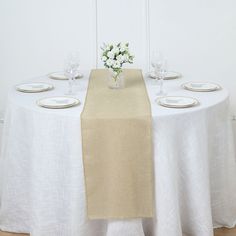 the table is set with white plates and green napkins on it, along with flowers in a vase