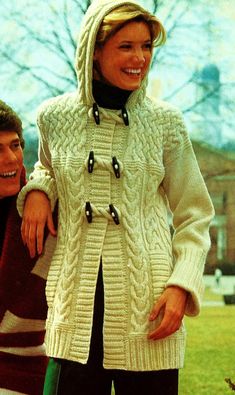 a man and woman standing next to each other in front of a tree wearing sweaters