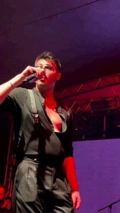 a woman singing into a microphone while standing in front of a purple stage with other people