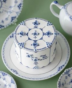 a blue and white cake sitting on top of a plate next to other plates, cups and saucers