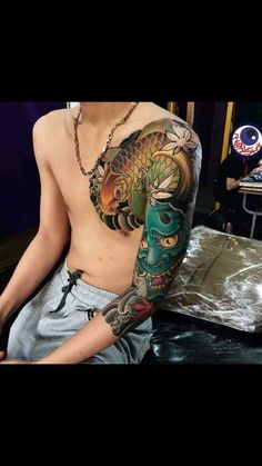 a man with a dragon tattoo on his arm and chest sitting in front of a mirror