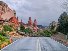 an empty road in front of some red rocks and trees on the other side with a building at the end