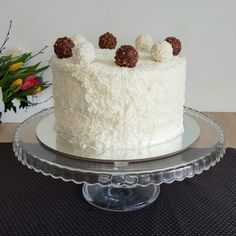 a cake with white frosting and chocolate toppings on a glass platter next to flowers